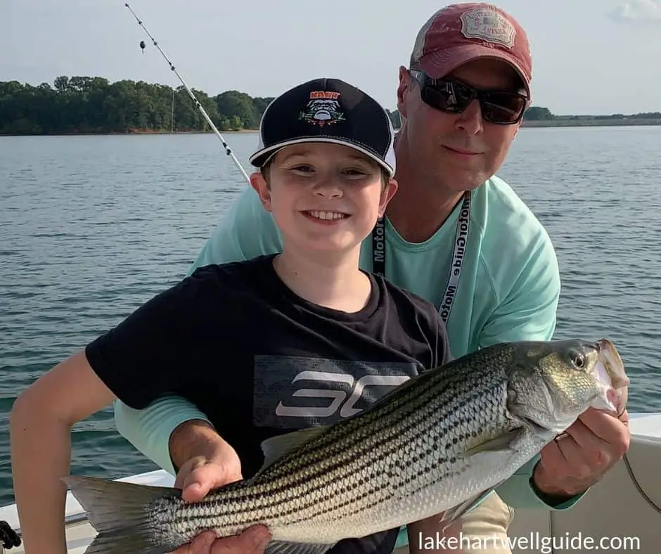 Father and son holding up large fish that they caught together on boat on Lake Hartwell, smiling at camera.